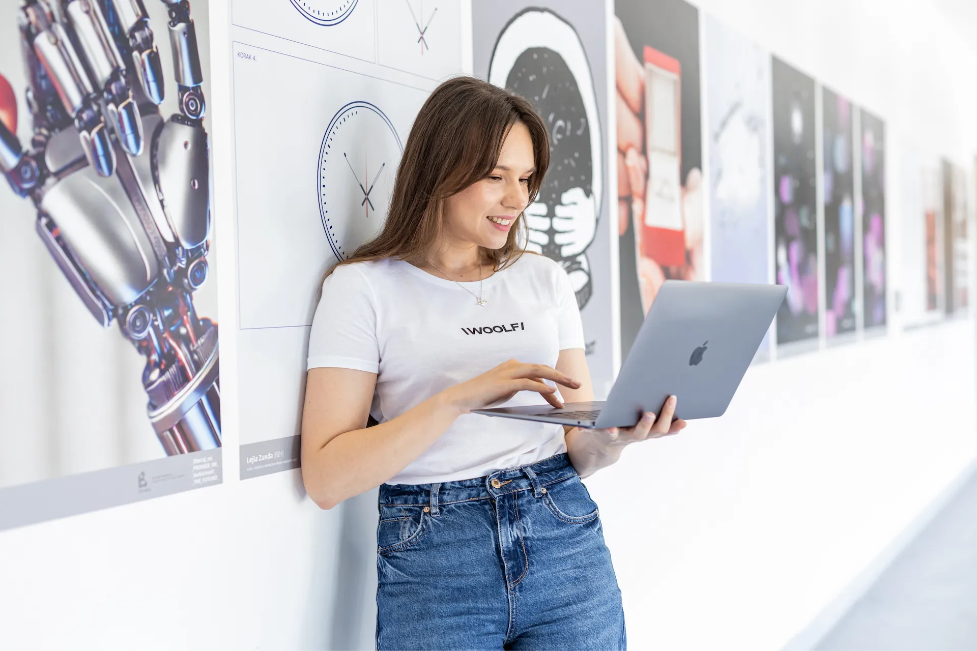 A woman wearing a white t-shirt with WOOLF logo on it holding a laptop