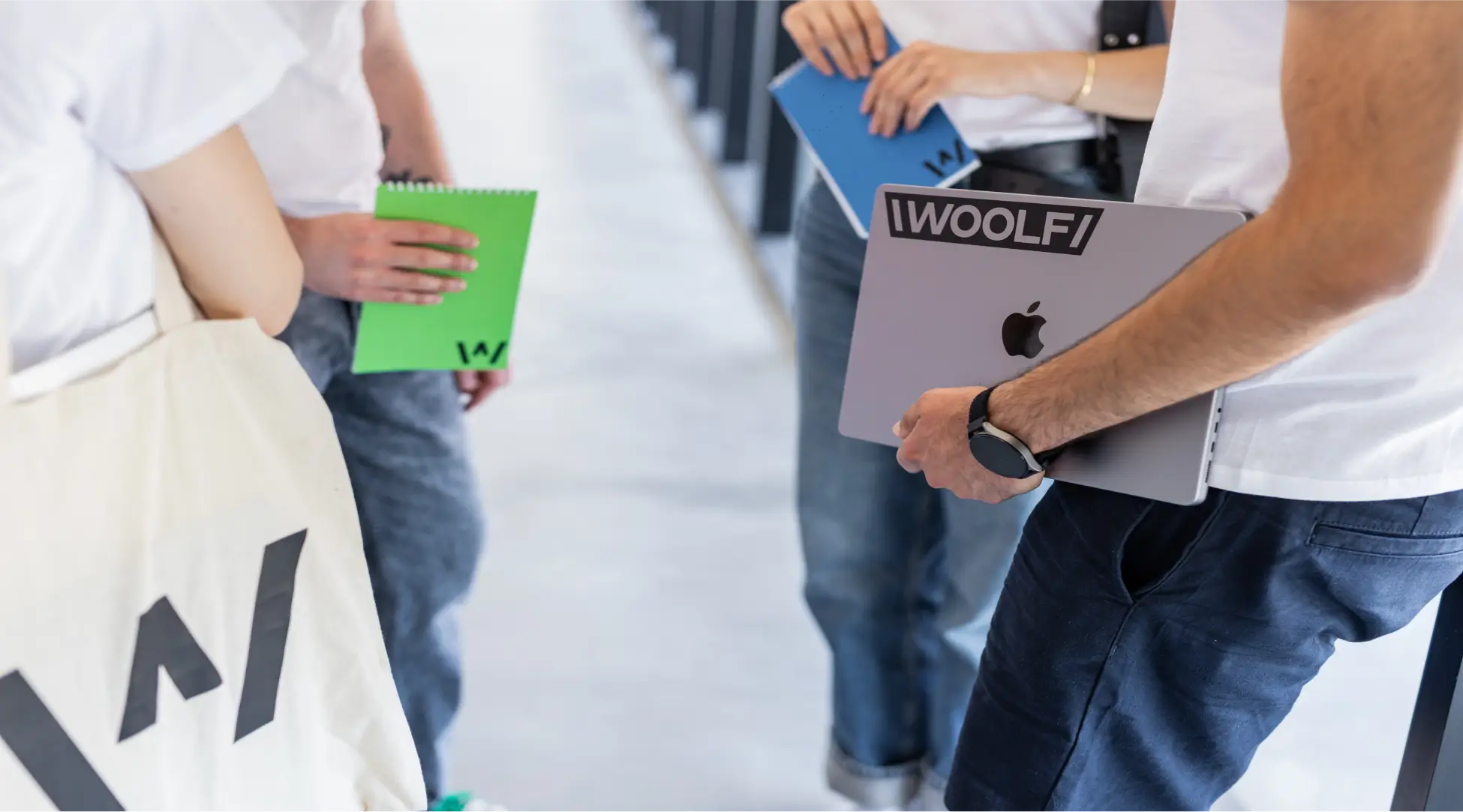 A person holding a macbook with woolf logo on it. Also a person is wearing Woolf bag